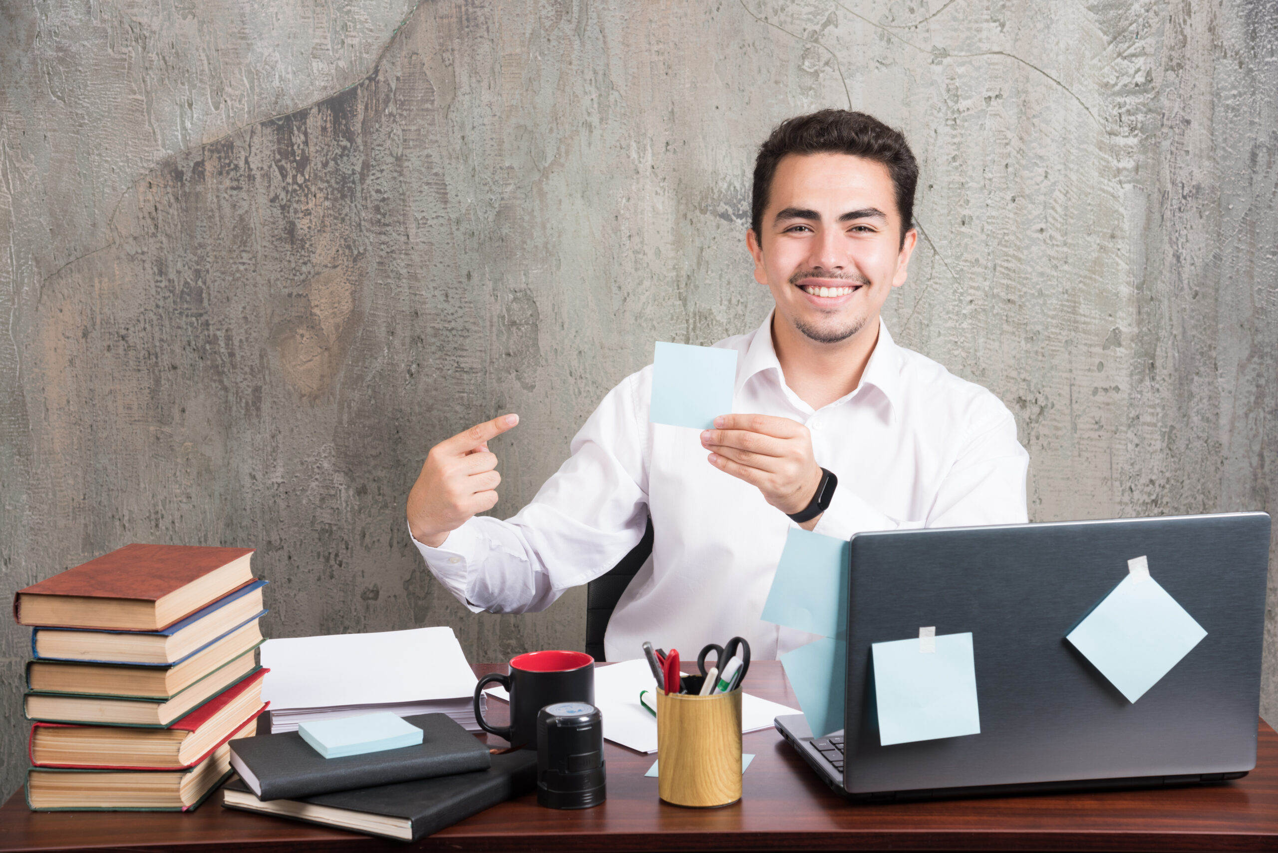 Young employee happily pointing his memo pad at the office desk. High quality photo